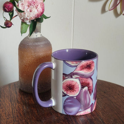Mug with fig design next to a vase with pink flowers on a wooden surface.