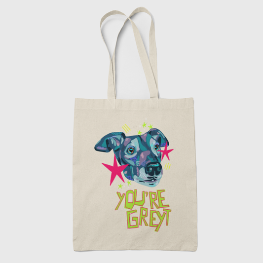 A beige canvas tote bag with a colorful graphic of a greyhound's face in blue, purple, and pink, surrounded by pink stars and the text 'YOU'RE GREY' in yellow-green lettering, shown against a light gray background.