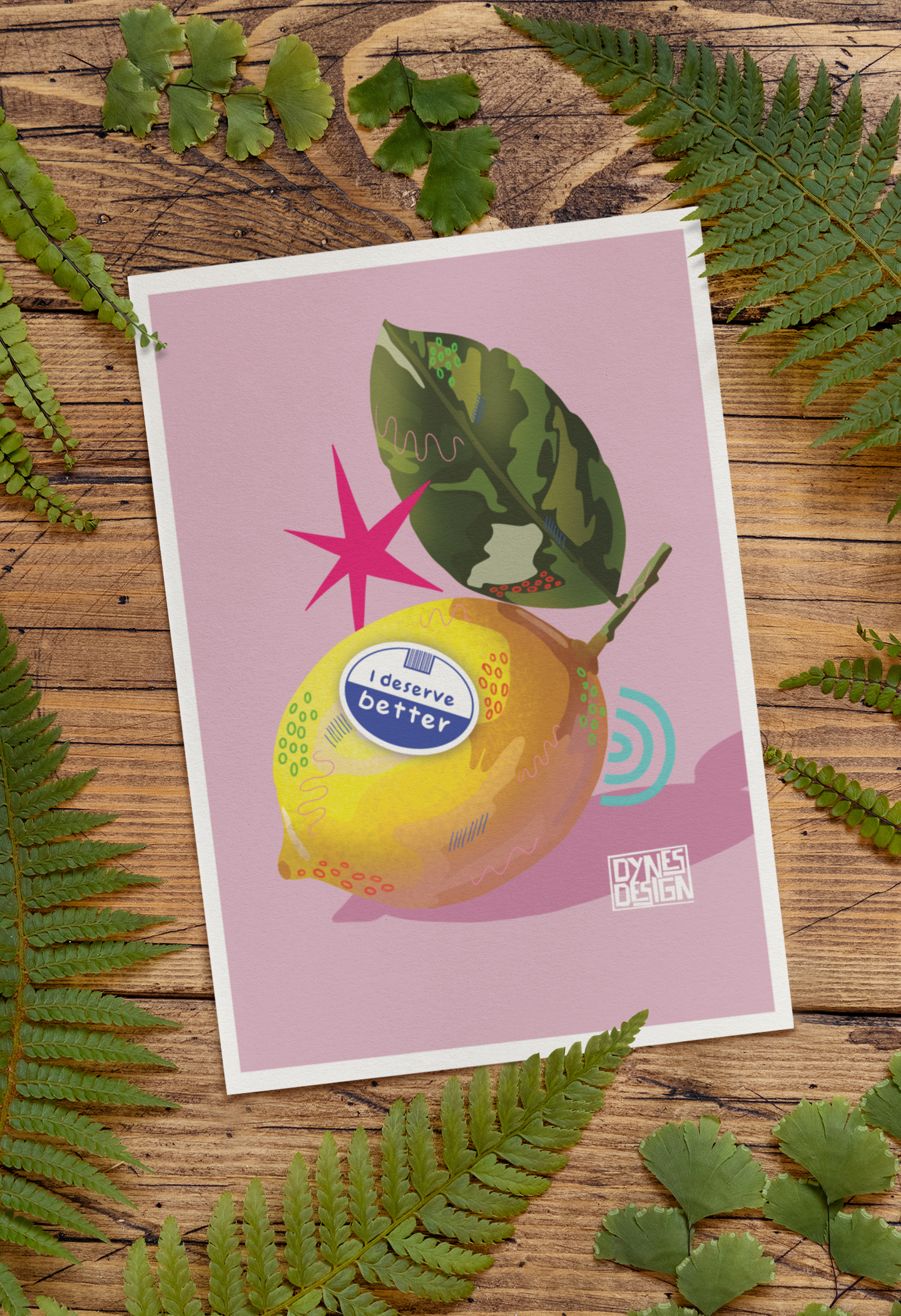 A square art print featuring a stylized illustration of a yellow lemon with a green leaf on a dusty pink background, styled flat-lay on a rustic wooden surface surrounded by green fern leaves. The lemon illustration includes a parody label reading 'I deserve better'.