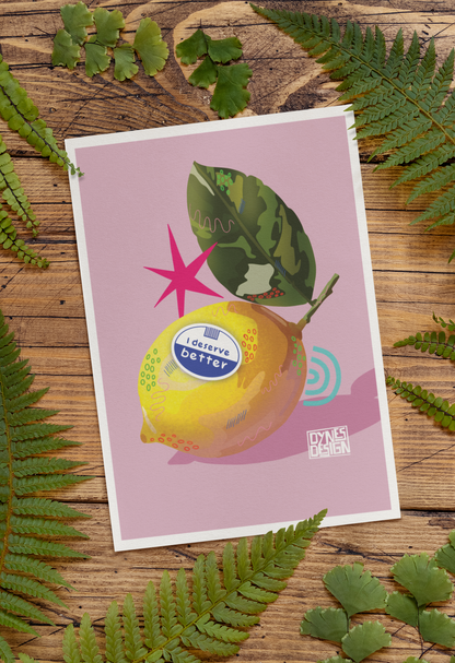 A square art print featuring a stylized illustration of a yellow lemon with a green leaf on a dusty pink background, styled flat-lay on a rustic wooden surface surrounded by green fern leaves. The lemon illustration includes a parody label reading 'I deserve better'.