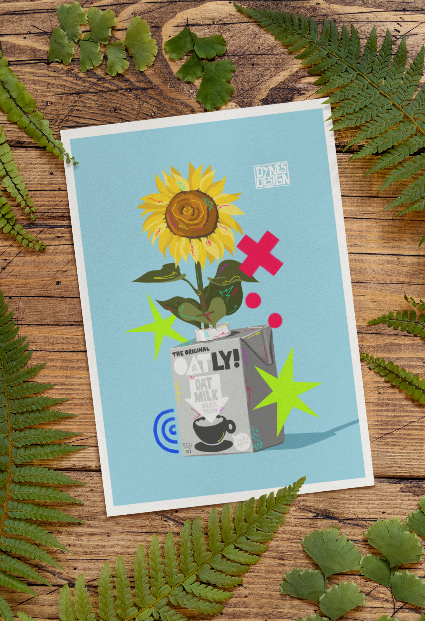 An art print with a white border lies on a rustic wooden surface, surrounded by green fern leaves. The print features a light blue background with a stylized illustration of a sunflower growing out of an oat milk carton, with abstract green and pink shapes.