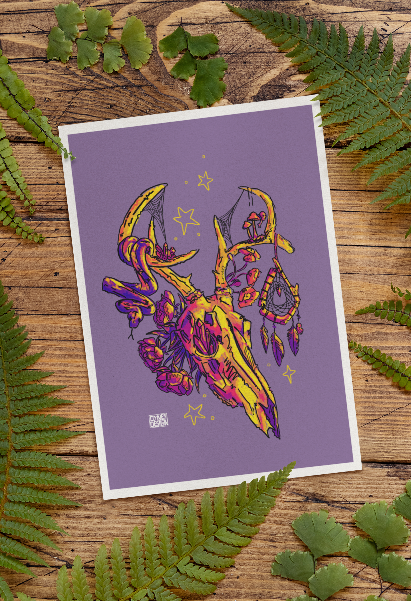 An art print with a white border featuring a purple background and a colorful illustration of a deer skull with a dreamcatcher, styled on a rustic wooden surface surrounded by green fern leaves.