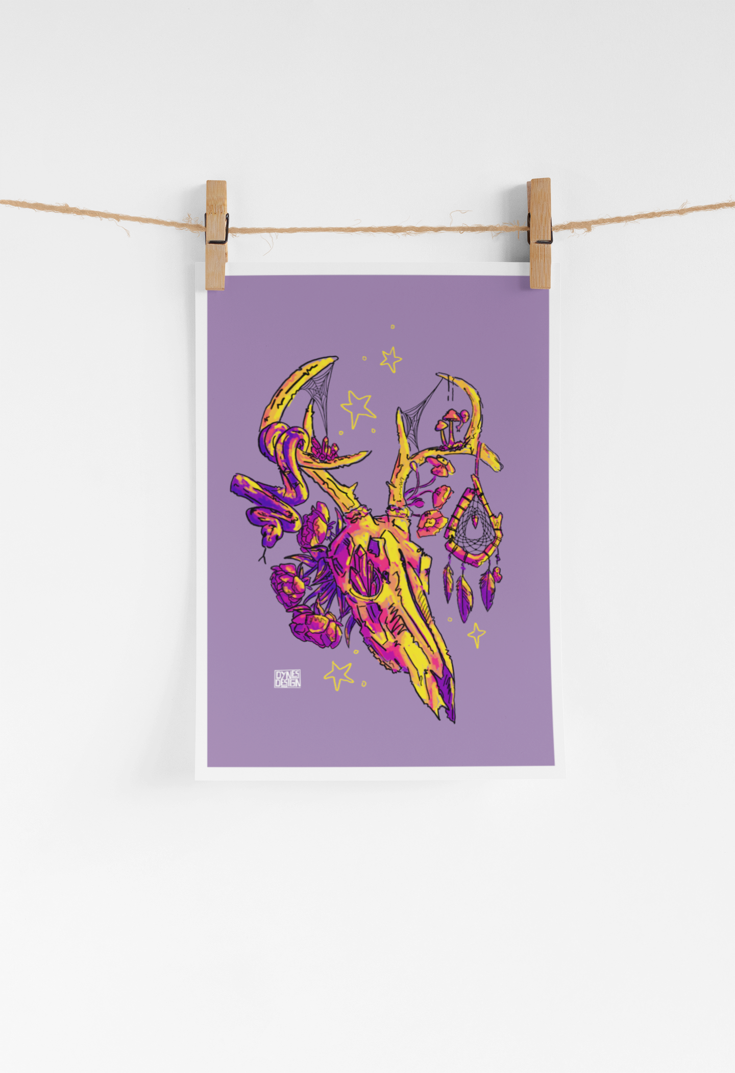 A vertical art print with a lavender-purple background featuring a stylized yellow and magenta deer skull illustration, hanging from a string with two wooden clothespins against a white wall.
