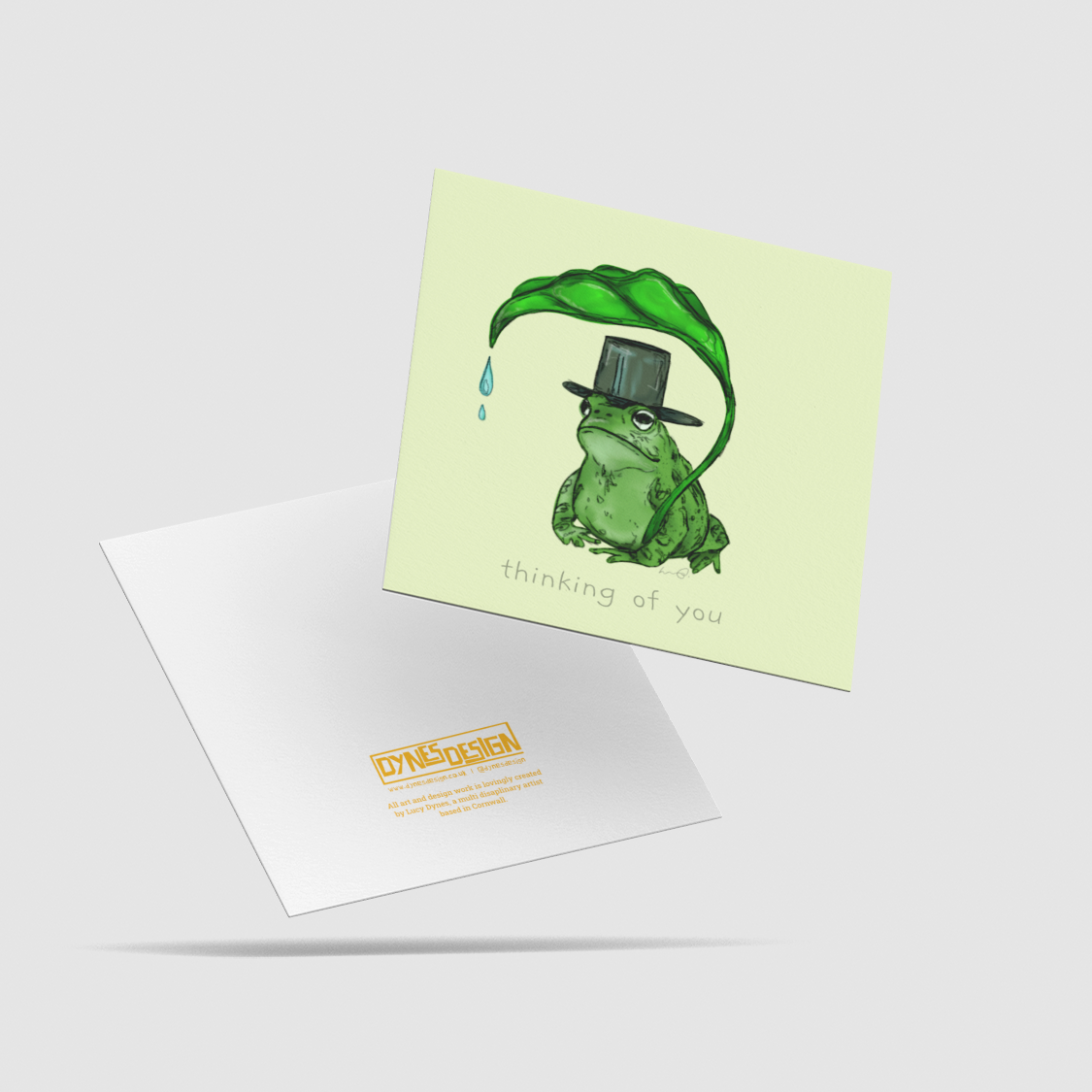 A back and front view of a card. The front has a digital illustration of a frog in a top hat, holding a leaf, with the words 'thinking of you'. The back features the logo mark "DYNES DESIGN". All floating on a light grey background.