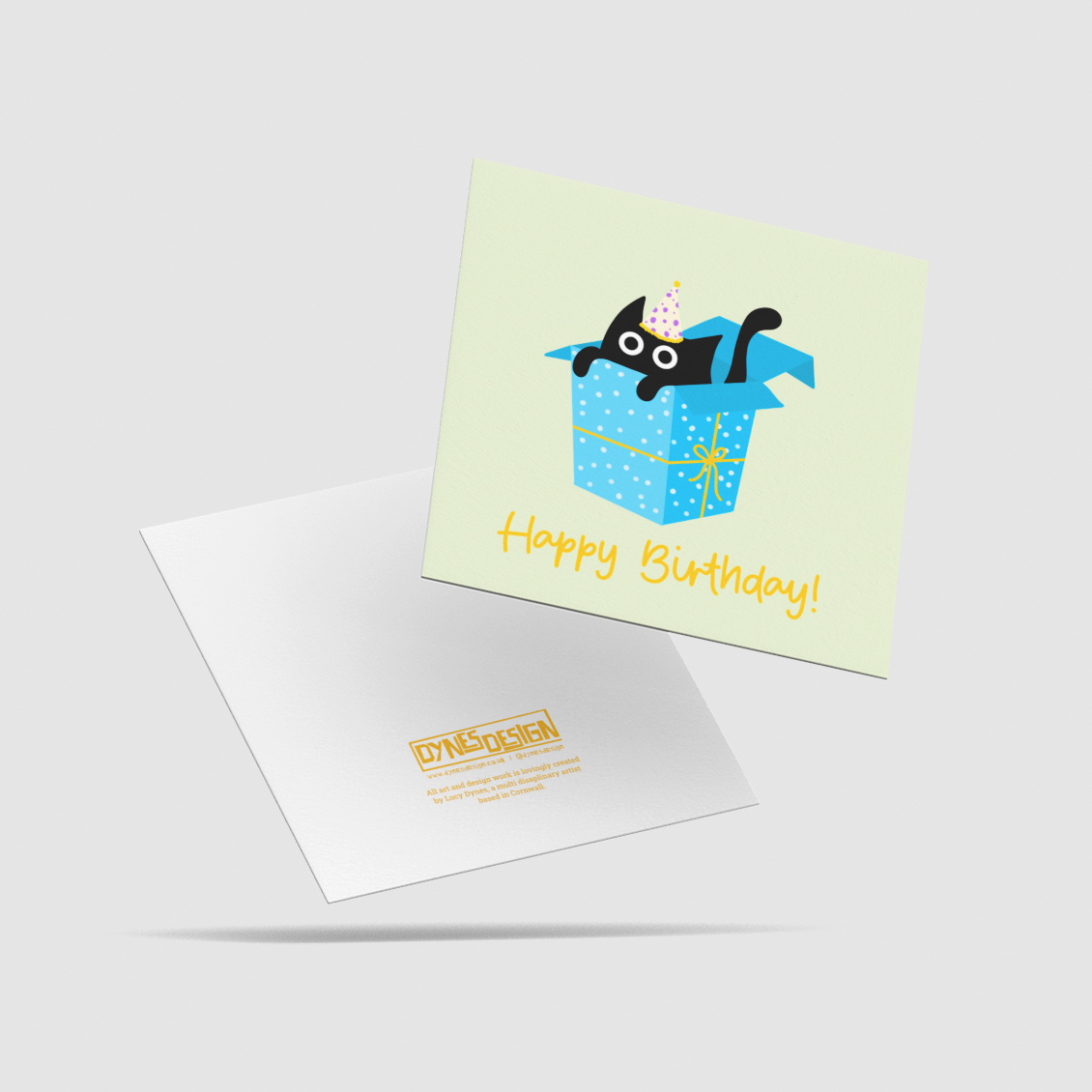 A square birthday card with another behind showing the back, shown on a light gray background. The card features a pale yellow-green background with a cartoon black cat peeking out of a blue gift box, and the words 'Happy Birthday!' in yellow.